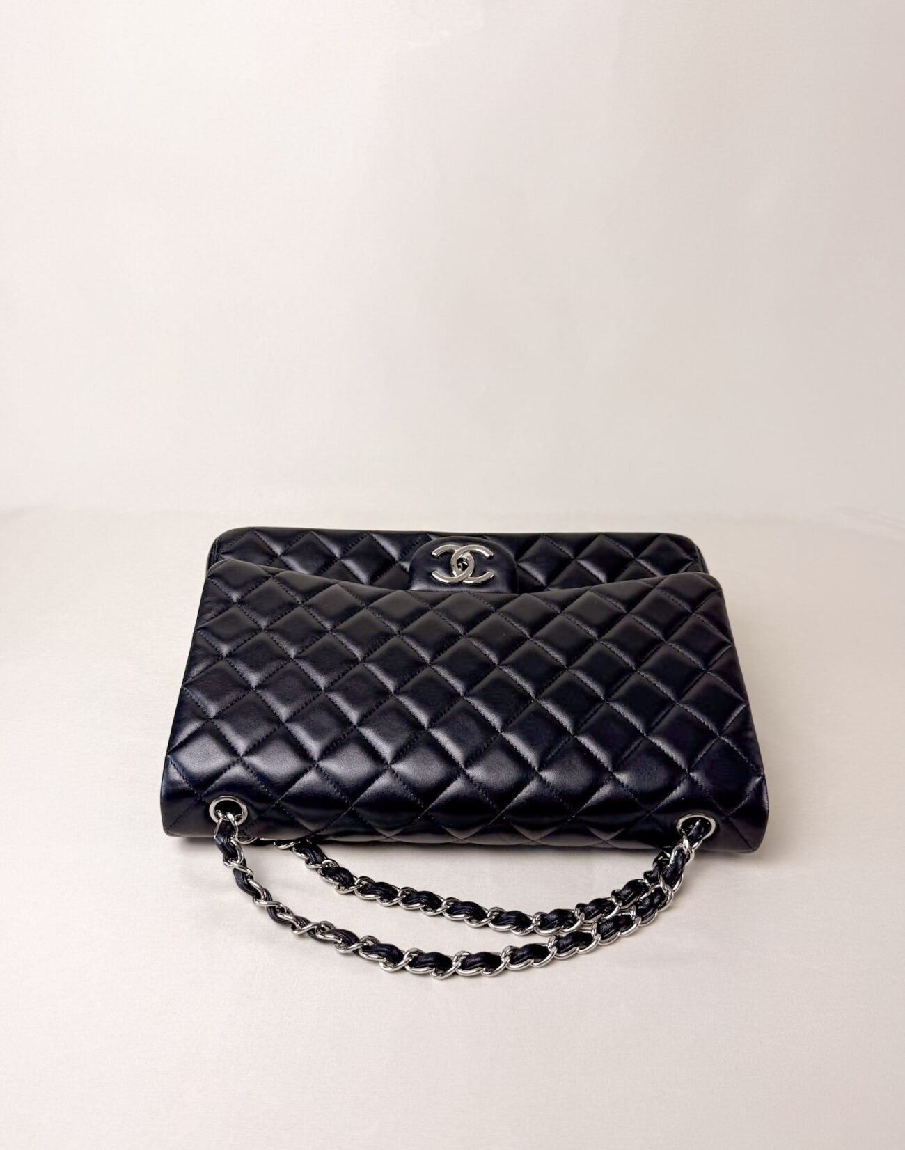 Side resting view of Chanel Classic Flap Maxi Jumbo Double Flap bag in black lambskin with palladium hardware