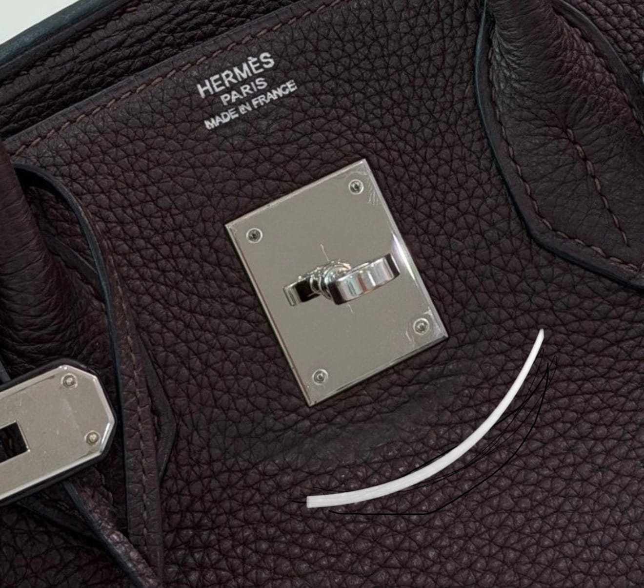 Smile mark developing beneath Hermès turnlock due to leather contraction and long-term tension around hardware.