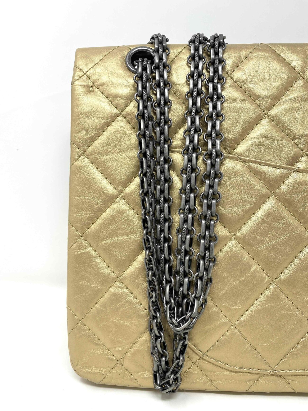 Close-up of Chanel 2.55 Reissue gold quilted calfskin bag with antique silver metal chain straps and eyelet hardware.