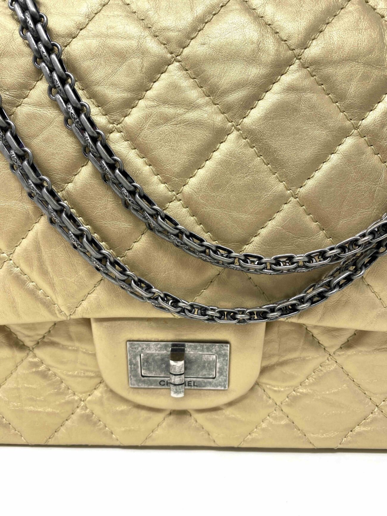 Close-up of Chanel 2.55 Reissue gold aged calfskin bag featuring the Mademoiselle turn-lock, antique silver chain and diamond-quilted leather.