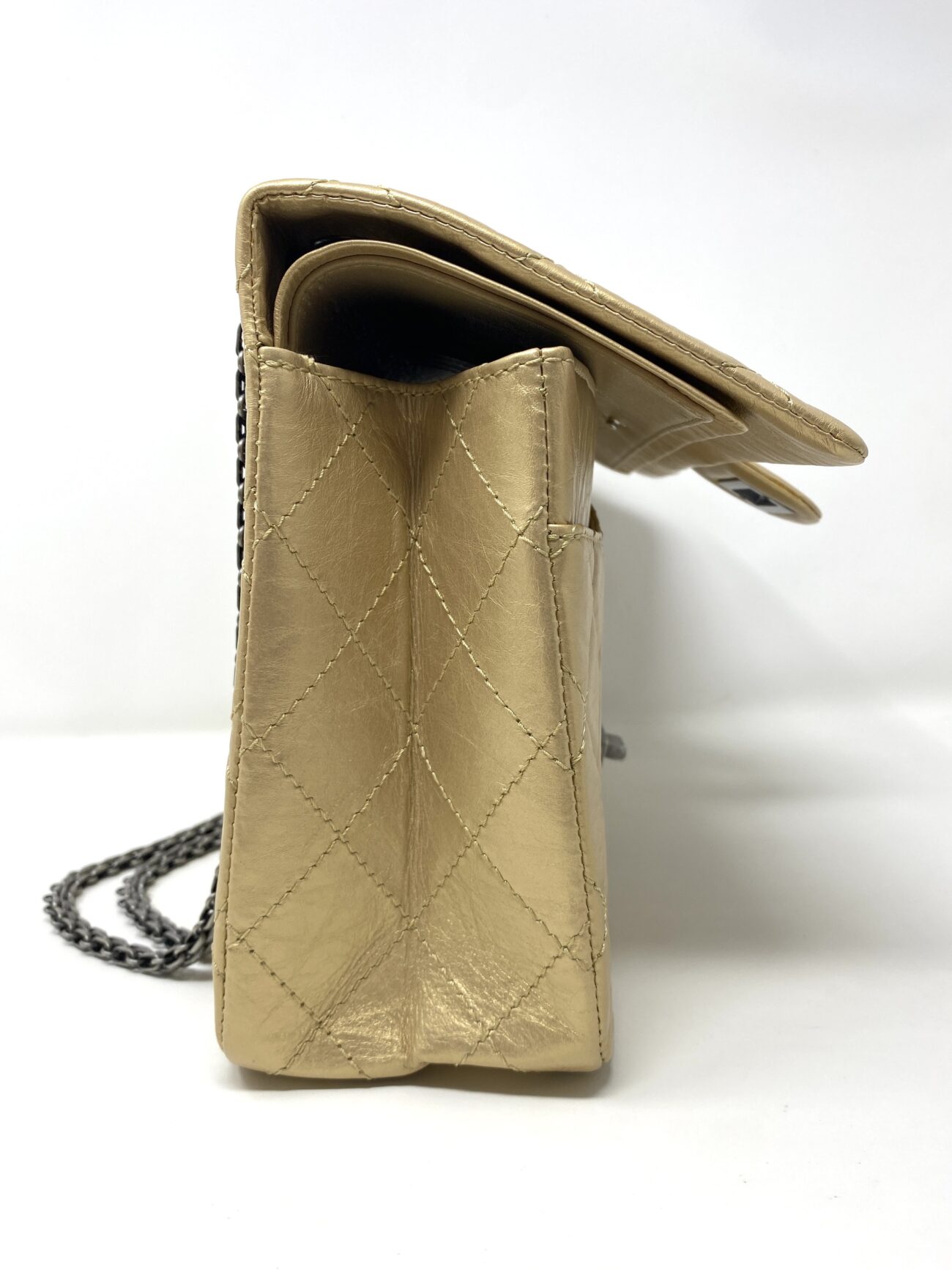 Side view of Chanel 2.55 Reissue gold aged calfskin bag with open double flap, diamond-quilted gusset and visible leather stitching.